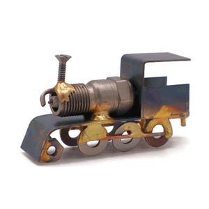 May include: A miniature train sculpture crafted from metal components. The train features a spark plug engine, a screw smokestack, and a dark blue and gold color scheme. The wheels are made from washers. The overall design is industrial and artistic.