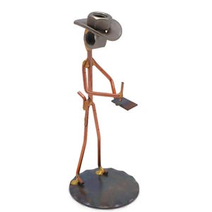 May include: A metal sculpture of a person wearing a cowboy hat and holding a notepad. The sculpture is made of copper wire and metal nuts and bolts. The person is standing on a round metal base.