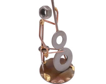 May include: A metal sculpture of a person playing a double bass. The person is made of copper wire and has a nut for a head. The double bass is made of two metal washers and a copper wire. The sculpture is standing on a round metal base.