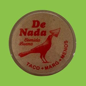 May include: A brown round sticker with red text that reads "De Nada" and "Comida Buena". A red bird with a beak is holding a red object in its beak. The text "Taco + Marg + Menos" is written in a circle around the bird.