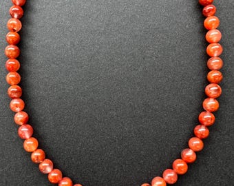 May include: A necklace made of red carnelian beads. The beads are round and have a smooth, polished finish. The necklace is strung on a thin, clear cord.