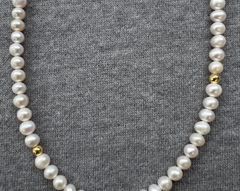 May include: A white pearl necklace with gold accents. The necklace is on a gray fabric background.
