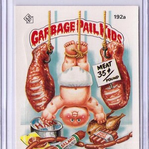 May include: A Garbage Pail Kids trading card featuring a baby with a white diaper hanging upside down with a rope tied around its ankles. The baby is surrounded by various meats, including a ham, a roast, and hot dogs. The card is titled "Delicate Tess" and has the text "Meat 35¢ Pound" on it.