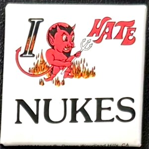 May include: Square white button with the words "I HATE NUKES" and a cartoon devil holding a pitchfork. The devil is red with black horns and is standing in front of flames.