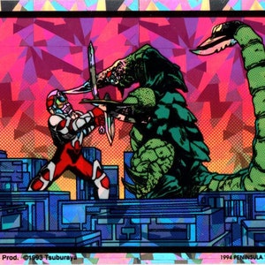 May include: A holographic sticker featuring a comic-style illustration of a battle between a red and white armored figure and a green monster with a long, segmented tail. The background includes a cityscape and a geometric pattern. The sticker has text at the bottom.