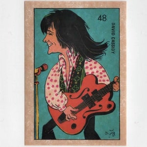 May include: A vintage trading card featuring a cartoon illustration of David Cassidy playing a red electric guitar. The card is blue with white lettering and the number 48.