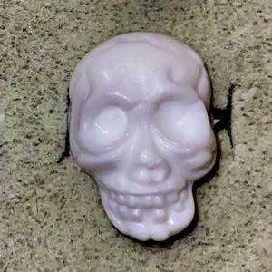 May include: A white ceramic skull with a detailed face, including eye sockets, a nose, and a mouth with teeth. The skull is a decorative item.