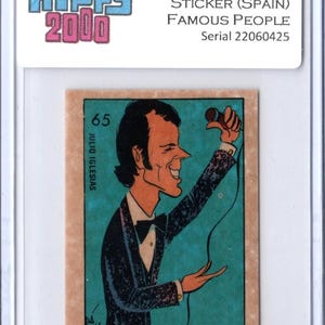 May include: A vintage trading card featuring a cartoon illustration of Julio Iglesias. The card is from the 1973 Hippy 2000 Famous People series, with the text "STICKER (SPAIN)". The card has a teal background and a tan border, encased in a protective sleeve.