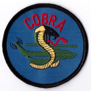 May include: A blue and black embroidered patch with a red cobra and the word "COBRA" above it. The cobra is coiled around a green helicopter.
