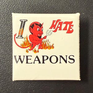 May include: Square button with a devil illustration. The red devil figure holds a trident and is surrounded by flames. The text reads "I HATE WEAPONS" in red and black.