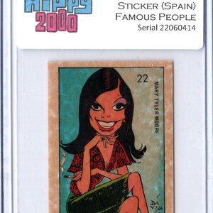 May include: A vintage 1973 Hippy 2000 sticker from Spain featuring a cartoon illustration of Mary Tyler Moore. The sticker has a serial number of 22060414 and is encased in a protective holder. The illustration depicts a woman with dark hair, a red top, and a green skirt.