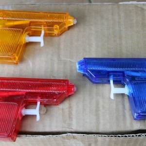 May include: Three plastic toy water guns in different colors: yellow, red, and blue. The guns are all the same size and shape, and they have a simple design.