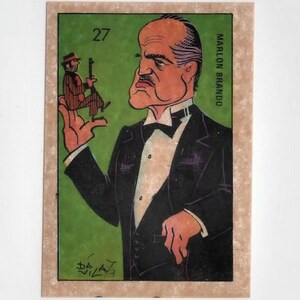May include: A caricature of Marlon Brando in a black tuxedo with a white bow tie and a white shirt. He is holding a small caricature of a man in his right hand. The background is green. The text "MARLON BRANDO" is printed on the right side of the image and the number "27" is printed in the top left corner.