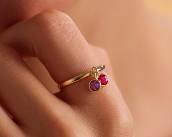 May include: A gold ring with two dangling charms. The charms are small, round, and red.