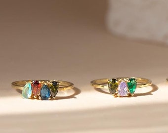 May include: Four gold rings with different colored gemstones. Each ring has two pear-shaped gemstones. The gemstones are red, green, blue, and purple.