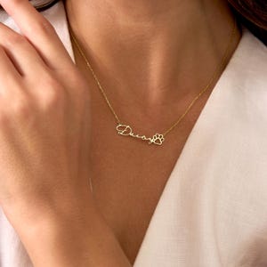 Pu&ograve; includere: Una delicata collana dorata con il nome "Daisy" in corsivo, seguito da un ciondolo a forma di zampa. La collana &egrave; mostrata su uno sfondo bianco, evidenziando il design e il colore del gioiello.