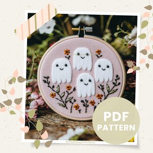 May include: A pink embroidery hoop with a design of four white ghosts with smiling faces and orange flowers. The hoop is surrounded by greenery and the text "PDF PATTERN" is written in white on a beige background.