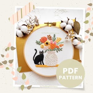 May include: Embroidery hoop art featuring a black cat and a vase of colorful flowers. The flowers include orange, yellow, and green hues. The vase is beige, and the cat is sitting on a yellow shelf. The text "PDF PATTERN" is in a circle.