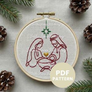 Puede incluir: Un bastidor de bordado con un diseño navideño de la Natividad, bordado en hilo rojo. El diseño incluye a María, José y el niño Jesús, con un corazón y una estrella dorados. El texto "PDF PATTERN" está en un círculo en la parte inferior derecha.