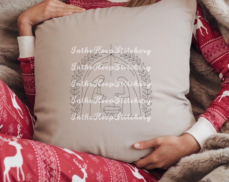 May include: A beige pillow with a black line drawing of the nativity scene inside a wreath. The text "In the Hoop Stitchery" is repeated around the image.