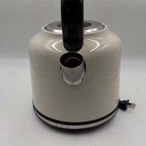 May include: Cream-colored electric kettle with a black handle and base trim. The kettle has a rounded body and a spout. A black power cord with a plug is visible.
