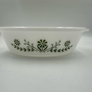 May include: White oval serving bowl with a green floral design. The bowl has a simple, elegant shape with a slightly flared rim and handles. The floral pattern features stylized flowers and leaves, adding a touch of nature to the kitchenware.