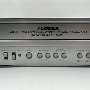 May include: Silver Lorex 1280 HR time-lapse recorder with digital shuttle. Features include a 40-hour real-time recording capability, menu, shift, and speed controls. The unit has a time-lapse function and audio on/off options.