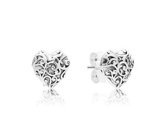 May include: A pair of silver heart-shaped stud earrings. Each earring features an intricate, openwork design of swirling patterns. The earrings are displayed on a white background, with their reflections visible below.