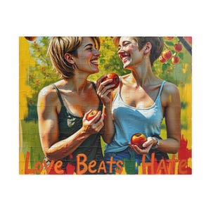 May include: Two women are smiling and holding red apples in a field with a yellow background. The text "Love Beats Hate" is at the bottom of the image.