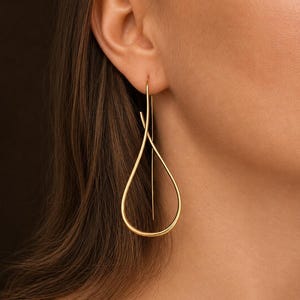 Peut inclure: Une boucle d'oreille dorée composée d'un long fil fin formant une boucle en forme de goutte allongée. Le design est constitué d'une seule pièce de métal continue qui passe à travers le lobe de l'oreille, créant une silhouette épurée.