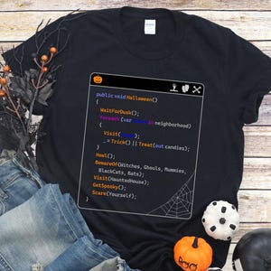 May include: Black t-shirt with a Halloween-themed code snippet graphic. The code includes phrases like "WaitForDusk" and "Treat (out candies)". The image also features blue jeans, decorative pumpkins, and a black and white striped ball.
