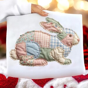 May include: A white pillow featuring a patchwork bunny design. The bunny is made of various pastel fabrics, including floral, gingham, and solid patterns. The bunny's ears and body are stitched together, creating a charming, handcrafted look.