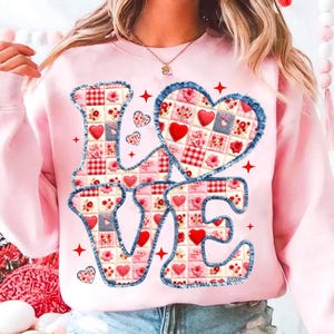 May include: Pink sweatshirt with the word "LOVE" in a patchwork design. The letters are outlined in denim and filled with red hearts and floral patterns. Small hearts and red stars are scattered around the letters.