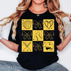 May include: Black t-shirt with a yellow checkered pattern featuring softball-themed graphics, including a glove, ball, bats, and bows.