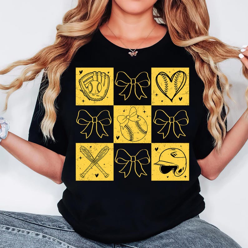 May include: Black t-shirt with a yellow checkered pattern featuring softball-themed graphics, including a glove, ball, bats, and bows.