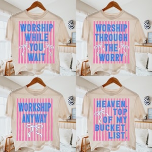 以下が含まれることがあります： さまざまなテキストデザインの4つのベージュTシャツ。各シャツには、垂直のピンクのストライプと青いテキストの長方形のデザインがあります。シャツのテキストは次のとおりです。「WORSHIP WHILE YOU WAIT」、「WORSHIP THROUGH THE WORRY」、「WORKSHOP ANYWAY」、および「HEAVEN. TOP OF MY BUCKET. LIST.」