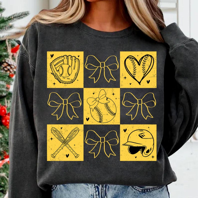 May include: Black sweatshirt with a yellow checkered pattern featuring softball-themed illustrations, including a glove, ball, bats, bows, and a heart.