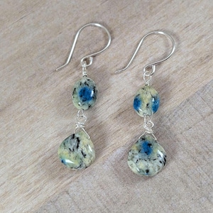 May include: A pair of silver dangle earrings with blue and white speckled stone beads. The earrings are made with wire wrapped beads.