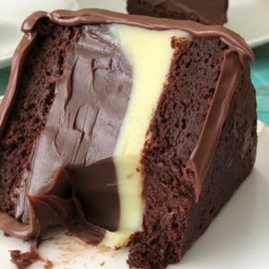 Op de afbeelding: Een plak chocoladetaart met een witte chocoladevulling. De taart is bedekt met chocolade glazuur en er is een hap uit genomen.