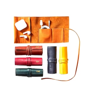 Può includere: Un organizer tecnologico in pelle arancione con tasche per accessori e diversi organizer per cavi arrotolati in pelle rossa, marrone, verde, blu navy e gialla. Ogni rotolo è fissato con un cinturino in pelle abbinato e presenta le iniziali.