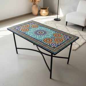 May include: Rectangular coffee table with a mosaic tile top. The tile features a geometric pattern in shades of teal, orange, and blue. The table has a black metal frame and measures approximately 47 inches long and 24 inches wide.