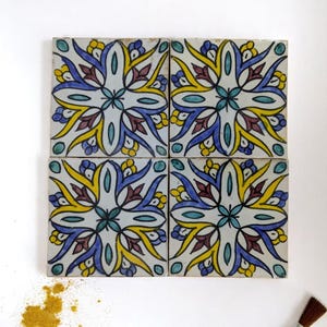 Peut inclure: Quatre carreaux de céramique carrés avec un motif floral jaune, bleu et turquoise. Les carreaux sont disposés ensemble, avec un pinceau et des pigments dispersés dans le coin.