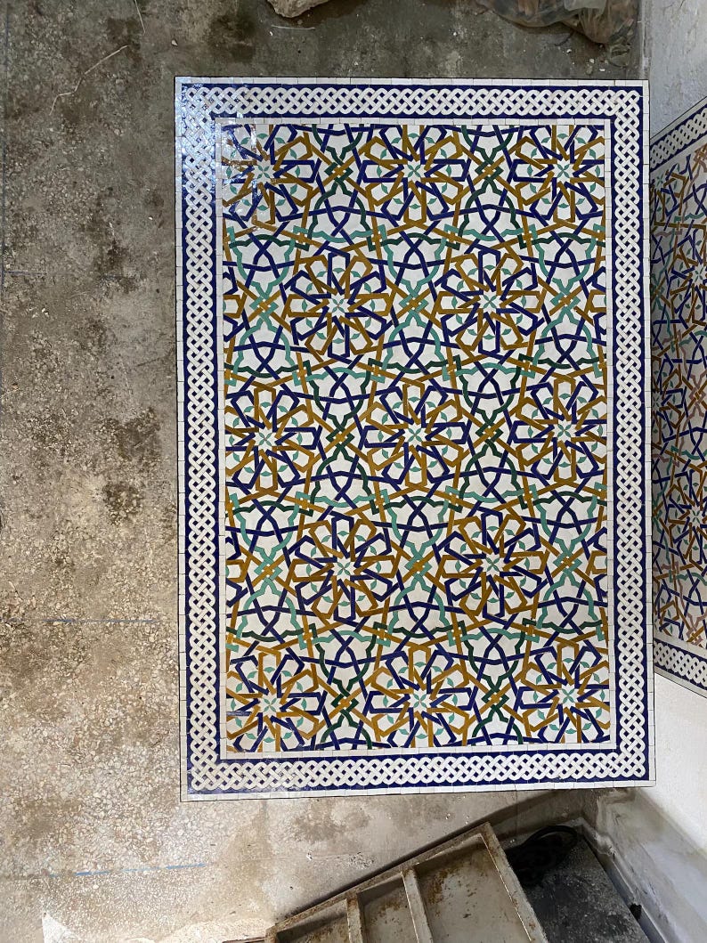 May include: A rectangular mosaic table top featuring a complex geometric pattern in shades of deep blue, mustard yellow, and teal green. The surface is bordered by a white and blue braided tile design, creating a repeating star-like motif.