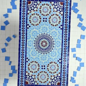 May include: A rectangular mosaic tile table with a detailed geometric pattern in shades of blue, brown, and purple. The table is surrounded by a dark blue border and features a central circular design. Scattered blue tiles are around the table.