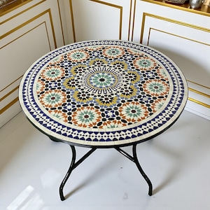 Könnte beinhalten: Runder Mosaiktisch mit schwarzem Metallgestell. Die Tischplatte weist ein farbenfrohes geometrisches Muster in Blau-, Orange-, Grün- und Gelbtönen auf. Der Tisch hat einen Durchmesser von etwa 76 cm.