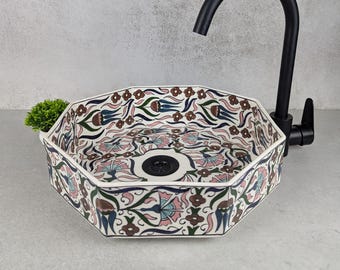 Puede incluir: Fregadero octogonal de cerámica con un patrón floral en tonos de rosa, azul, verde y marrón. El fregadero tiene un desagüe negro y se muestra con un grifo negro.