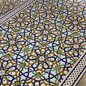 May include: A rectangular table surface featuring an intricate geometric mosaic pattern in shades of deep blue, mustard yellow, and forest green on a white background, framed by a white and blue braided border design across the entire top.