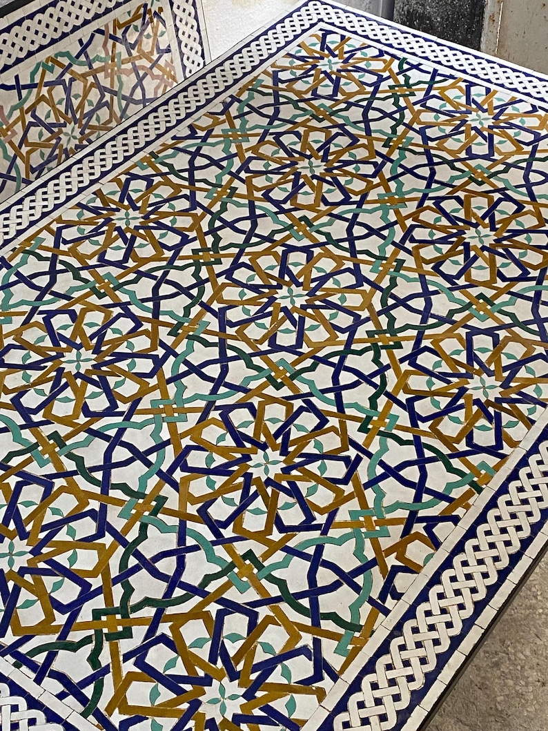 May include: A rectangular table surface featuring an intricate geometric mosaic pattern in shades of deep blue, mustard yellow, and forest green on a white background, framed by a white and blue braided border design across the entire top.