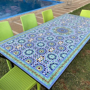 May include: A rectangular outdoor table with a mosaic tile top featuring a blue and white floral pattern. The table is supported by black metal legs and surrounded by four lime green chairs. The table is approximately 72 inches long.