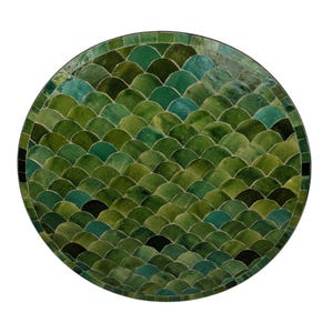 May include: A circular tabletop featuring a mosaic pattern of overlapping semi-circular tiles in various shades of green, ranging from deep forest green to light olive and teal, finished with a smooth, glossy surface and a dark circular border.